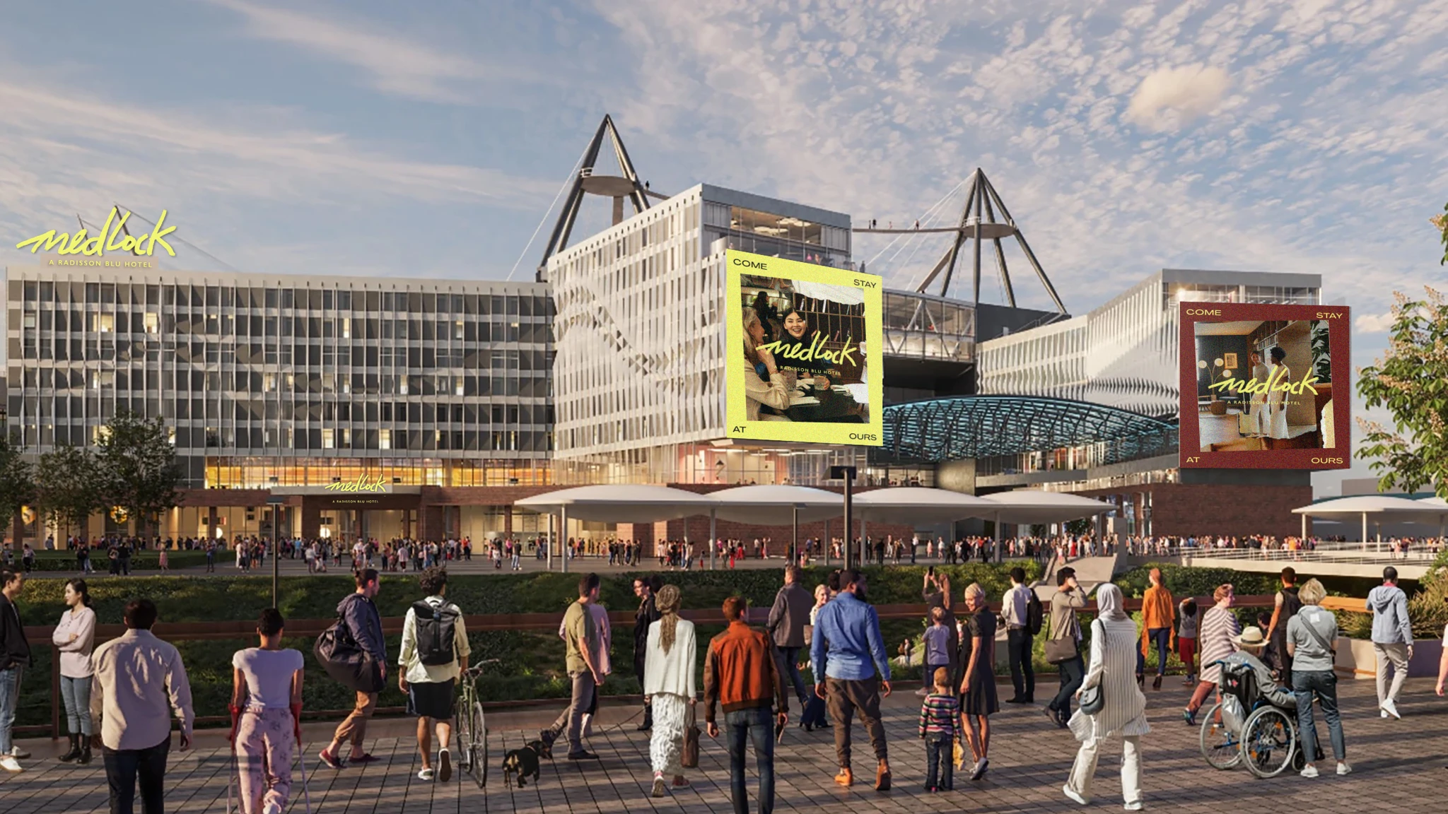 A large modern building labeled Medlock, with a crowd gathered in front and two large digital advertisements displayed. The scene suggests a public event or a popular venue, with many people walking towards it and standing in groups.